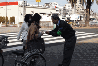 警察OBが歩道上で自転車盗難防止のためのパンフレットを配布している写真